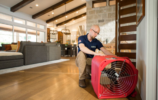 Worker using an industrial air mover to dry a wet space