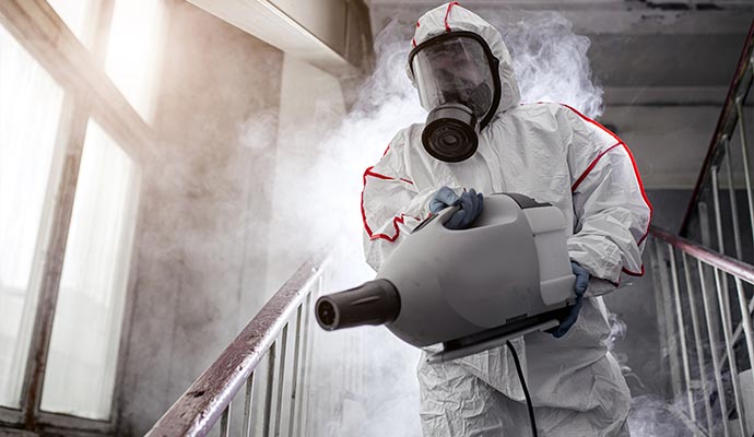 Man in a gas mask disinfecting stairs with a sprayer.